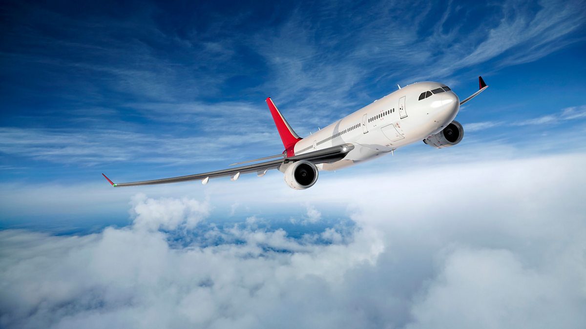 A commercial airplane with red winglets and tail, soaring above white clouds against a blue sky with wispy clouds, captures the excitement of journeys booked through your favorite travel agency.